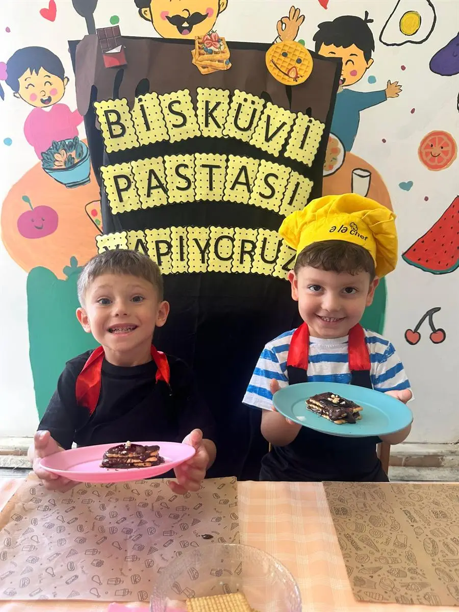 Aşçı önlükleriyle hazırladıkları bisküvi pastasını gösteren iki çocuk