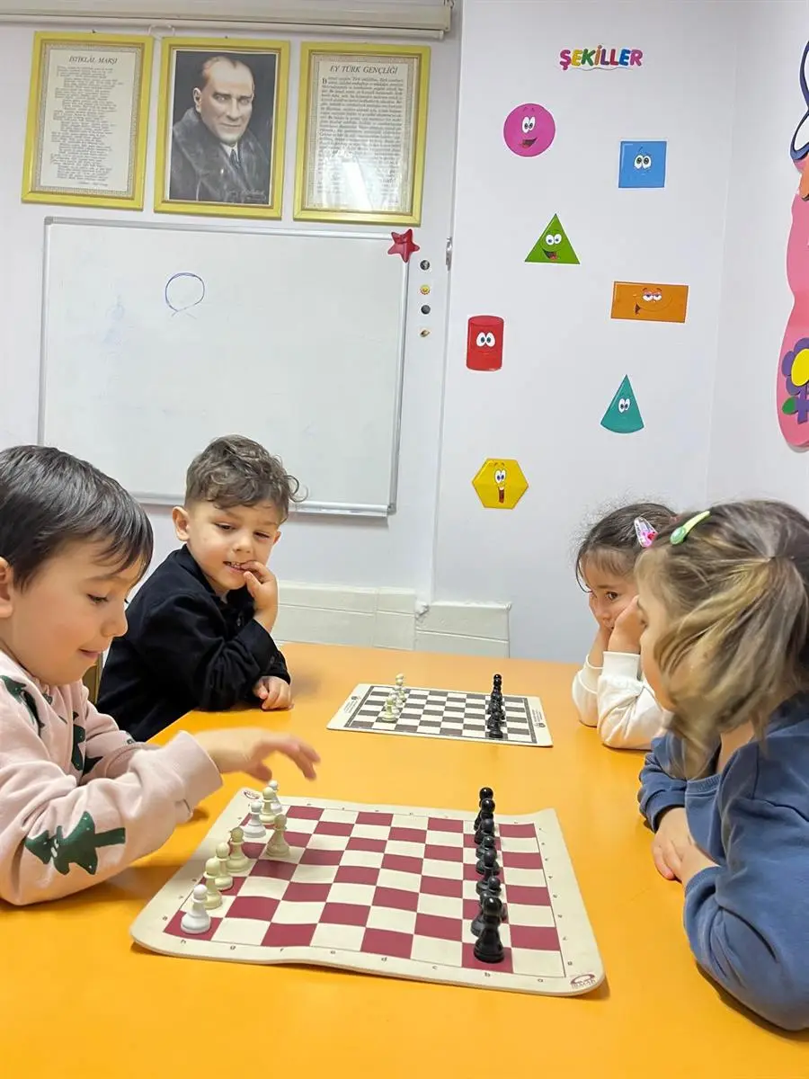 Sınıfta masa başında karşılıklı satranç oynayan dört çocuk
