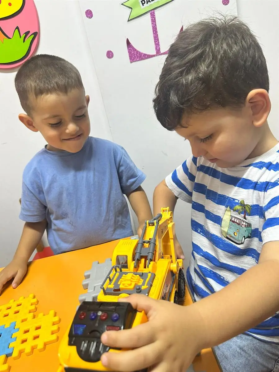 Masada uzaktan kumandalı oyuncak iş makinesiyle oynayan iki çocuk
